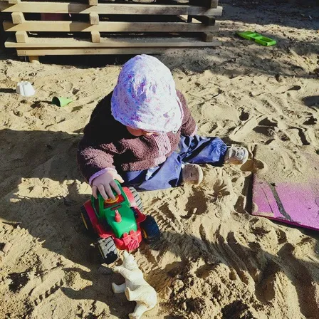 Ein kleines Kind spielt im Sand mit einem Spielzeuglastwagen und einem Spielzeugeisbären.