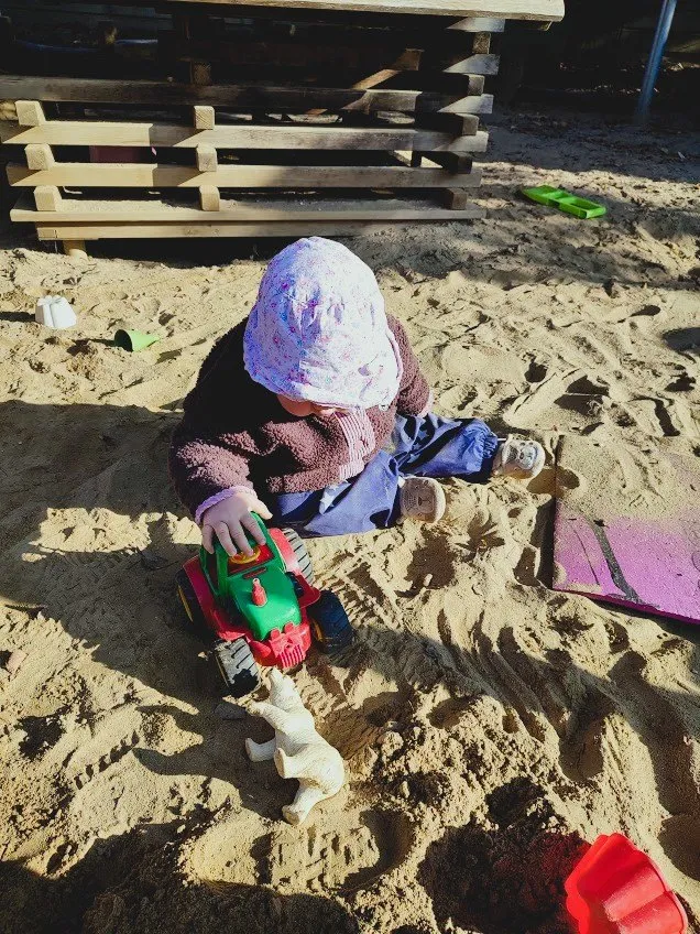 Ein kleines Kind spielt im Sand mit einem Spielzeuglastwagen und einem Spielzeugeisbären.