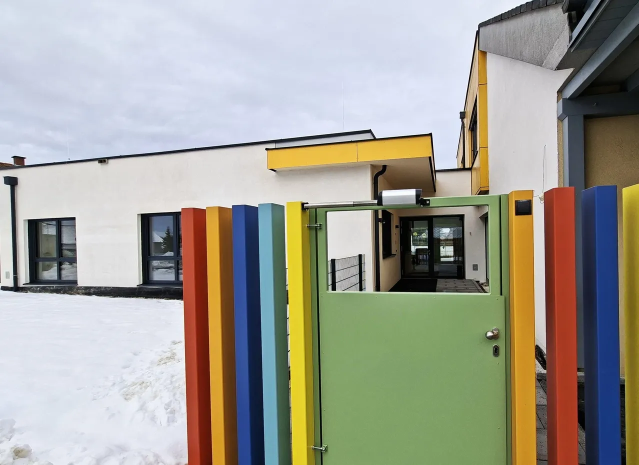 Ein farbenfrohes Haus mit einem Regenbogen-farbigen Zaun und einer grünen Tür mit Schloss und Griff, in einem verschneiten Gebiet gelegen.