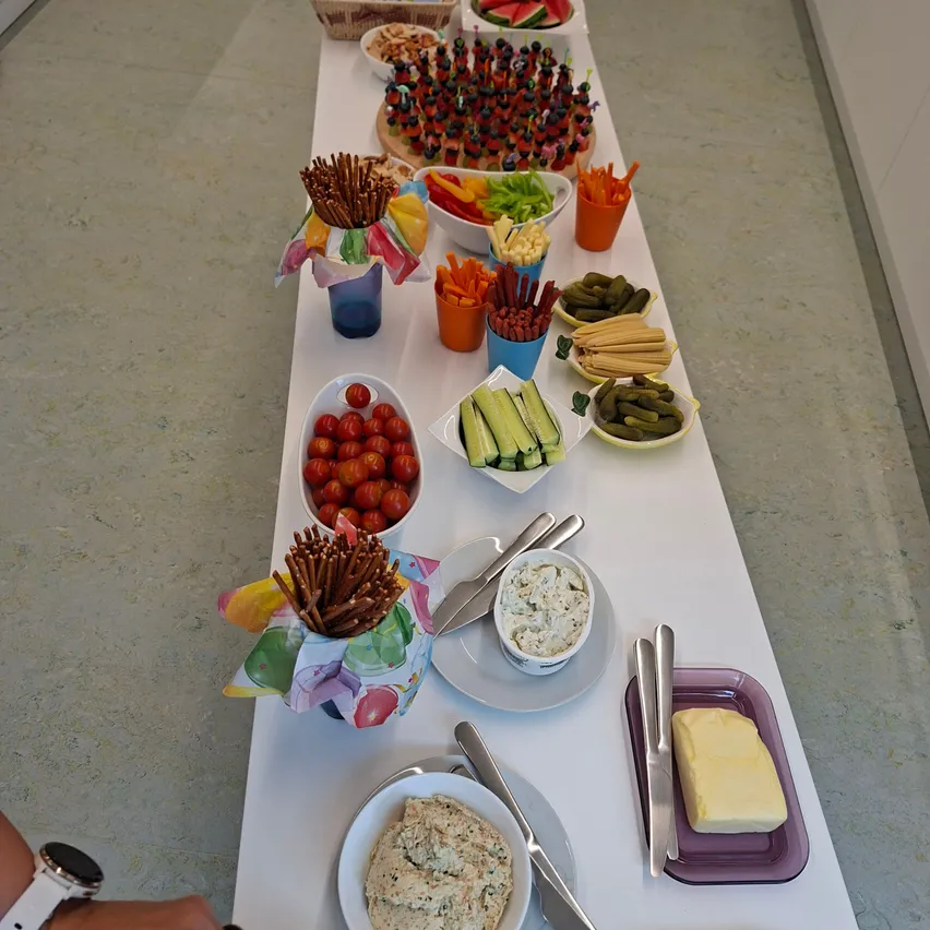 Ein langer Tisch, gefüllt mit verschiedenen Lebensmitteln wie Gemüse, Obst und Dips, in bunten Schüsseln und Tellern angeordnet.