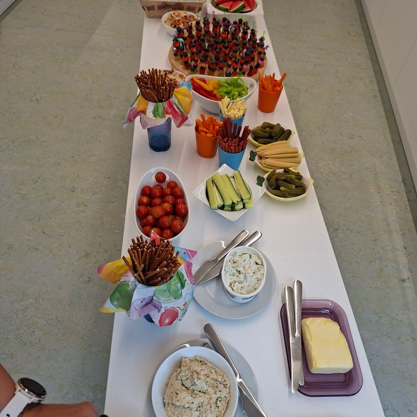 Ein langer Tisch, gefüllt mit verschiedenen Lebensmitteln wie Gemüse, Obst und Dips, in bunten Schüsseln und Tellern angeordnet.