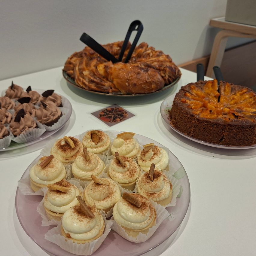 Ein Tisch mit vier Tellern mit Desserts: ein Schokoladenkuchen, ein Spiralgebäck, ein Schokoladencupcake und Cupcakes mit Sahne und Toppings.
