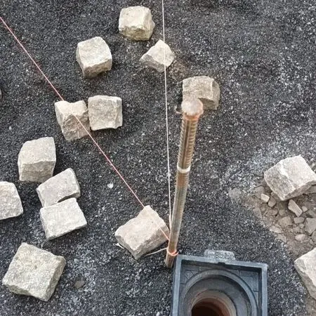 Baustelle mit Kies und einem Metallpfahl, möglicherweise zur Markierung oder Unterstützung, umgeben von verstreuten Steinen.