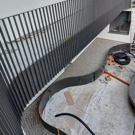 Ein Balkon mit einer geschwungenen Brüstung und verschiedenen Baumaterialien auf dem Boden, einschließlich eines schwarzen Schlauchs, Rohren und einer Leiter.