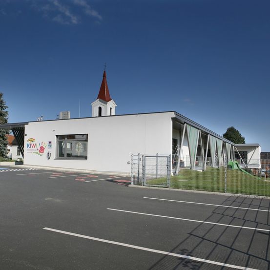 Ein weißes Gebäude mit einem roten Turm und einem Logo namens Kiwi, umgeben von einem Zaun und einem Parkplatz.