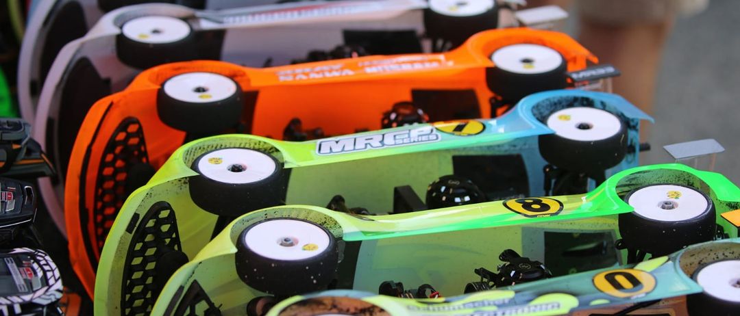 Mehrere Miniatur-Rennwagen in verschiedenen Farben und Designs sind aufgereiht und zeigen ihre Reifen, Räder und Sponsoren-Logos.