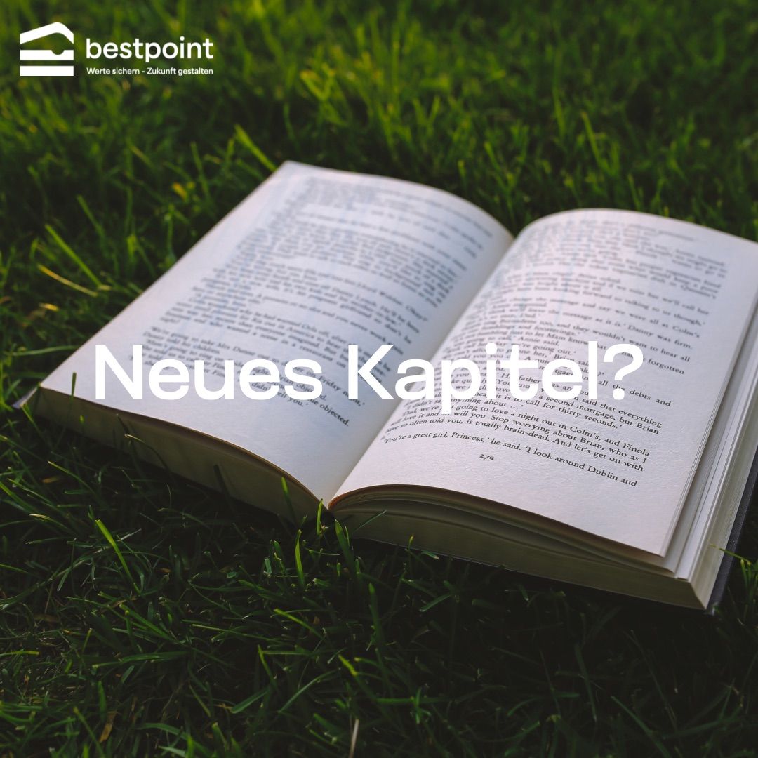 Ein offenes Buch mit dem Text Neues Kapitel? liegt auf grünem Gras. Das Buch ist auf eine Seite mit Text in einer fremden Sprache geöffnet.