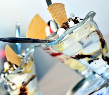 Drei Desserts mit Schlagsahne, Eis und Waffelkegeln. Löffel liegen obenauf.