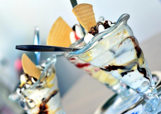 Drei Desserts mit Schlagsahne, Eis und Waffelkegeln. Löffel liegen obenauf.