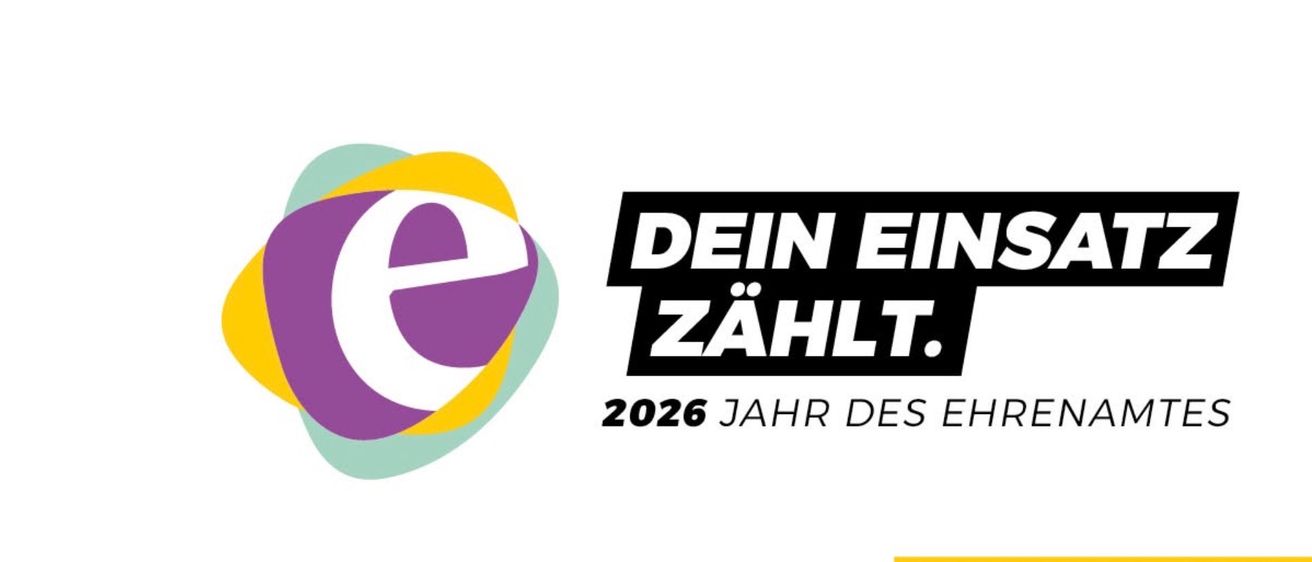 Das Bild zeigt ein Logo für das Jahr 2026. Es steht 'Deine Eingabe zählt' in fettem schwarzen Text. Das Logo ist kreisförmig mit einem mehrfarbigen Rand. Darunter befindet sich ein gelber Banner, der 'Engagiert. Im Jahr der Ehre' lautet.