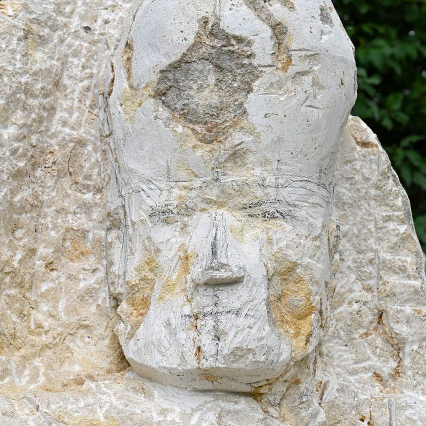 A weathered stone sculpture of a face, with distinct features like eyes, a nose, and a mouth, carved into a large rock.