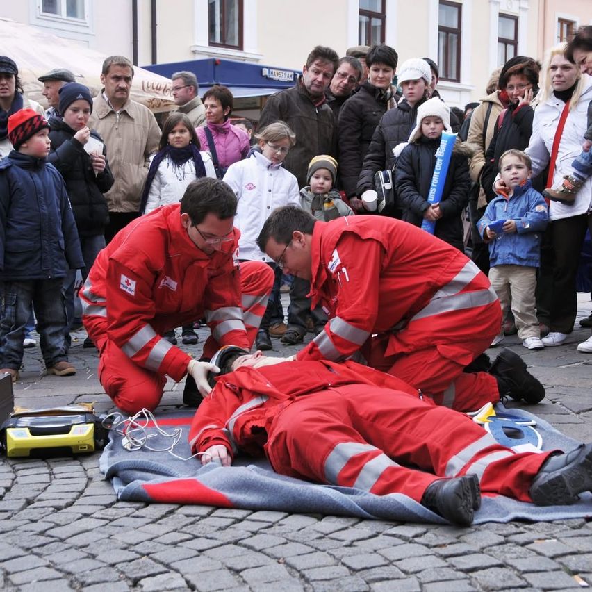 Two emergency workers are performing CPR on a man lying on the ground, with a crowd of people watching.