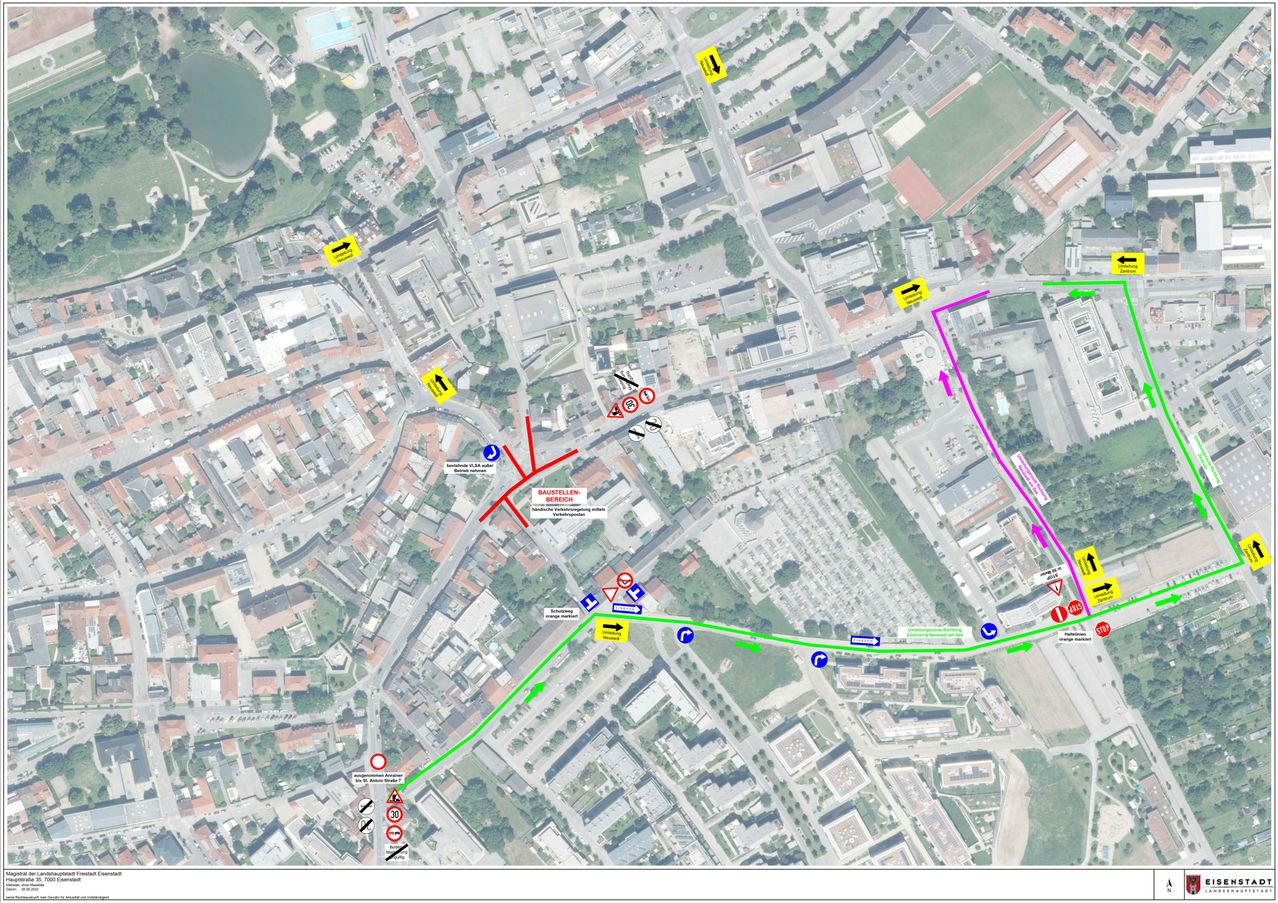 Eine Karte zeigt ein städtisches Gebiet mit verschiedenen Straßen und Schildern. Mehrere farbige Linien zeigen unterschiedliche Routen. Wichtige Kreuzungen und Orientierungspunkte sind markiert.