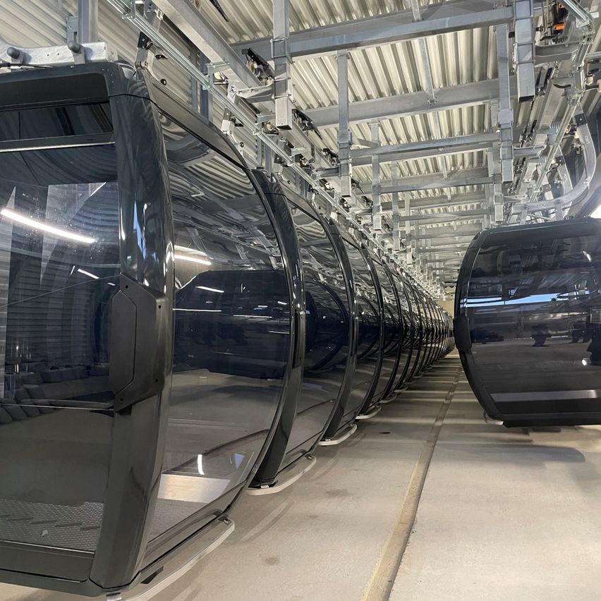 Mehrere schwarze Seilbahnen sind in einer Reihe aufgereiht. Sie sind leer und einsatzbereit. Die Seilbahnen sind an einer Metallstruktur befestigt.