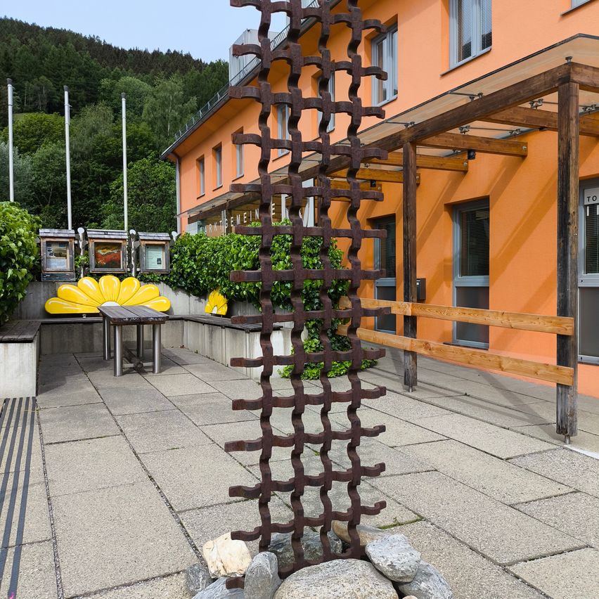 Ein orangefarbenes Gebäude mit einem Innenhof, einer hohen Metallskulptur und einem Tisch mit einer gelben Blume.