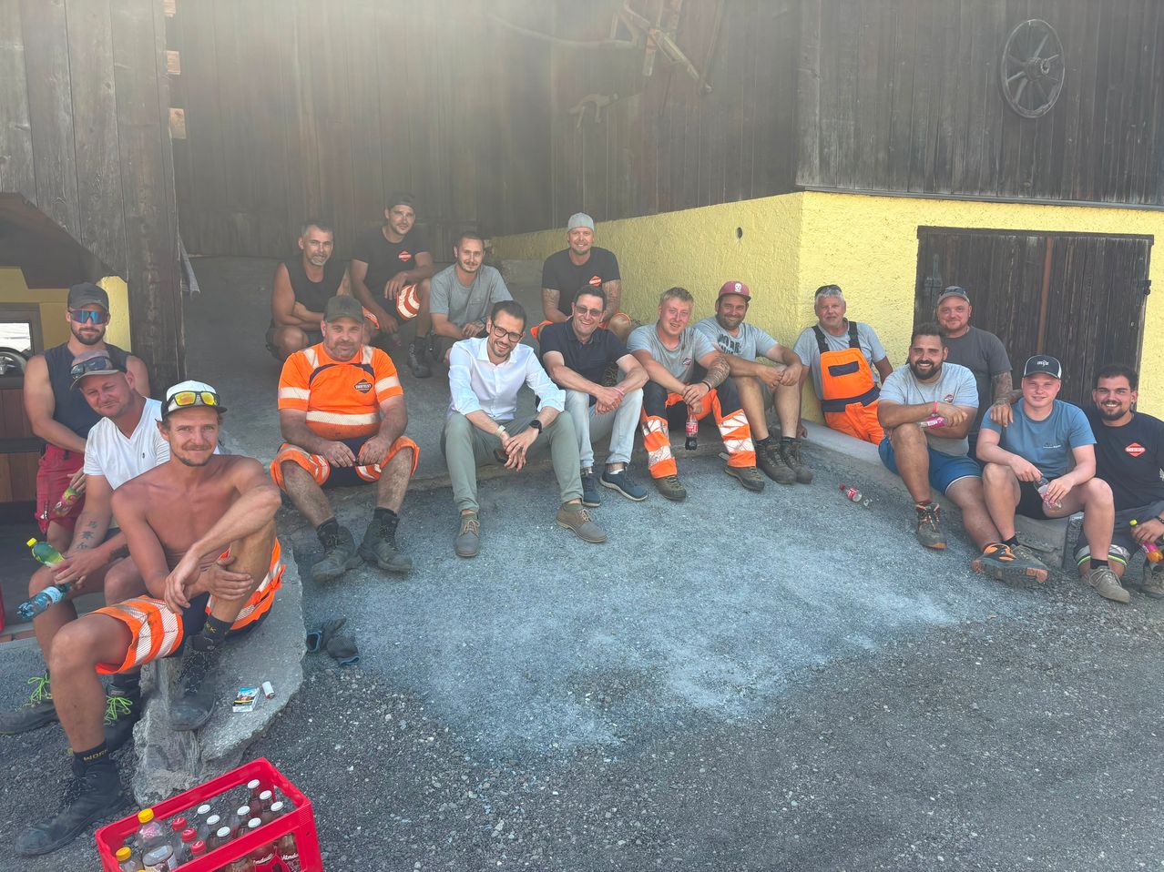 Eine Gruppe von Menschen in orangefarbenen Westen und Stiefeln, die auf dem Beton vor einem Gebäude sitzen und stehen, einige tragen Hüte.