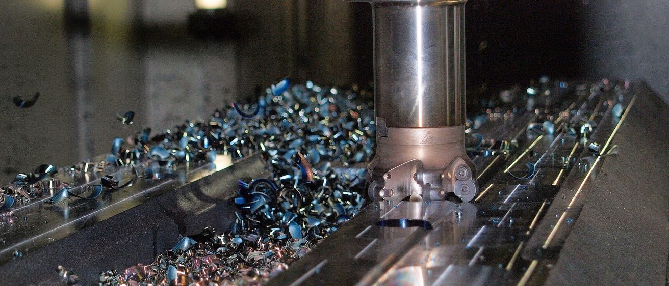 Eine Nahaufnahme einer Metallbearbeitungsmaschine im Einsatz, umgeben von verstreuten Metallspänen, mit einem hellen Licht im Hintergrund.