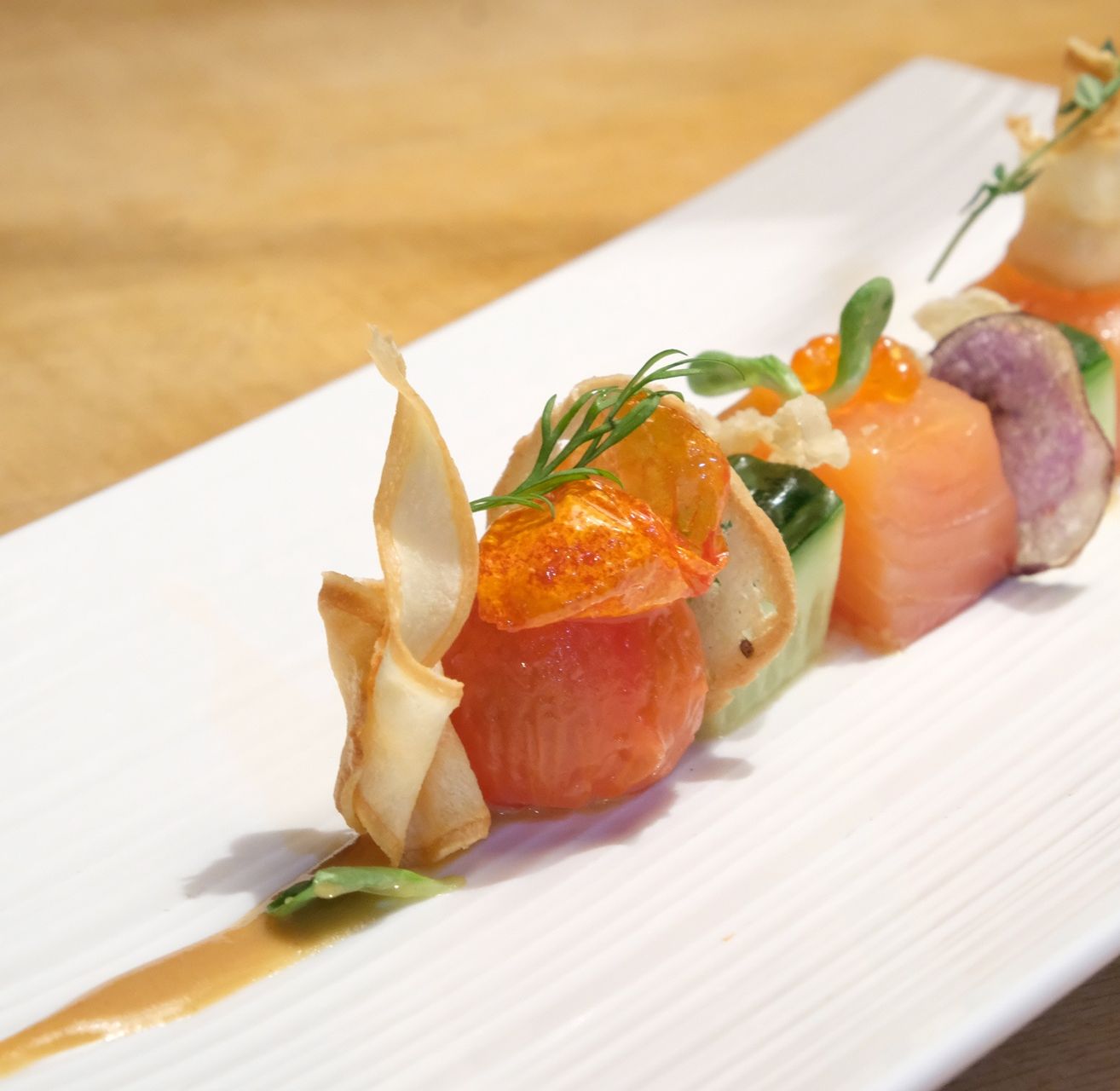 Ein Teller mit einer farbenfrohen Sashimi-Arrangement auf einem Holztisch, bestehend aus Lachs, Radieschen und Kräutern.