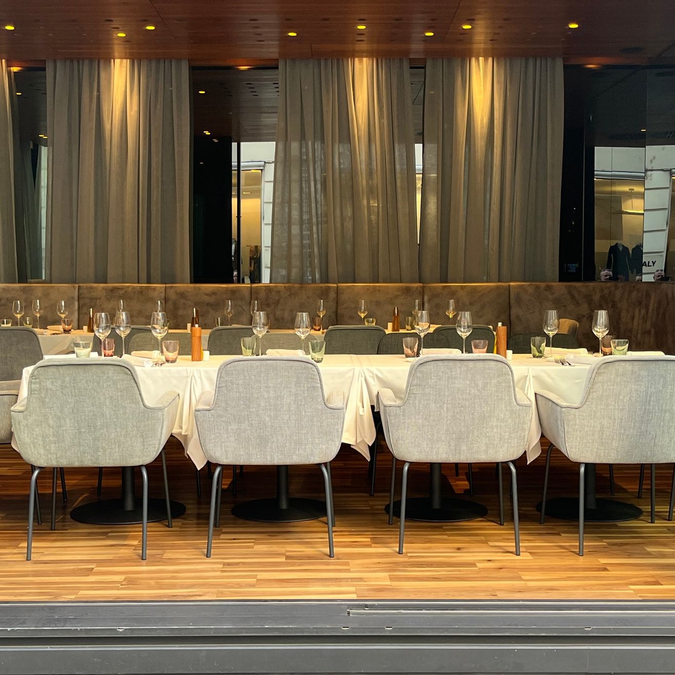 Ein elegantes Restaurant mit einem langen Tisch für das Essen. Die Stühle sind um den Tisch herum angeordnet, und es gibt Weingläser und andere Tischwaren. Der Raum ist mit Vorhängen dekoriert.