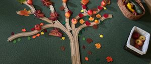 Ein grüner runder Teppich mit einem hölzernen Apfelbaum, umgeben von verschiedenen Früchten und Gemüse. Ein Korb mit Äpfeln und ein Korb mit Obst und Gemüse sind in der Nähe.