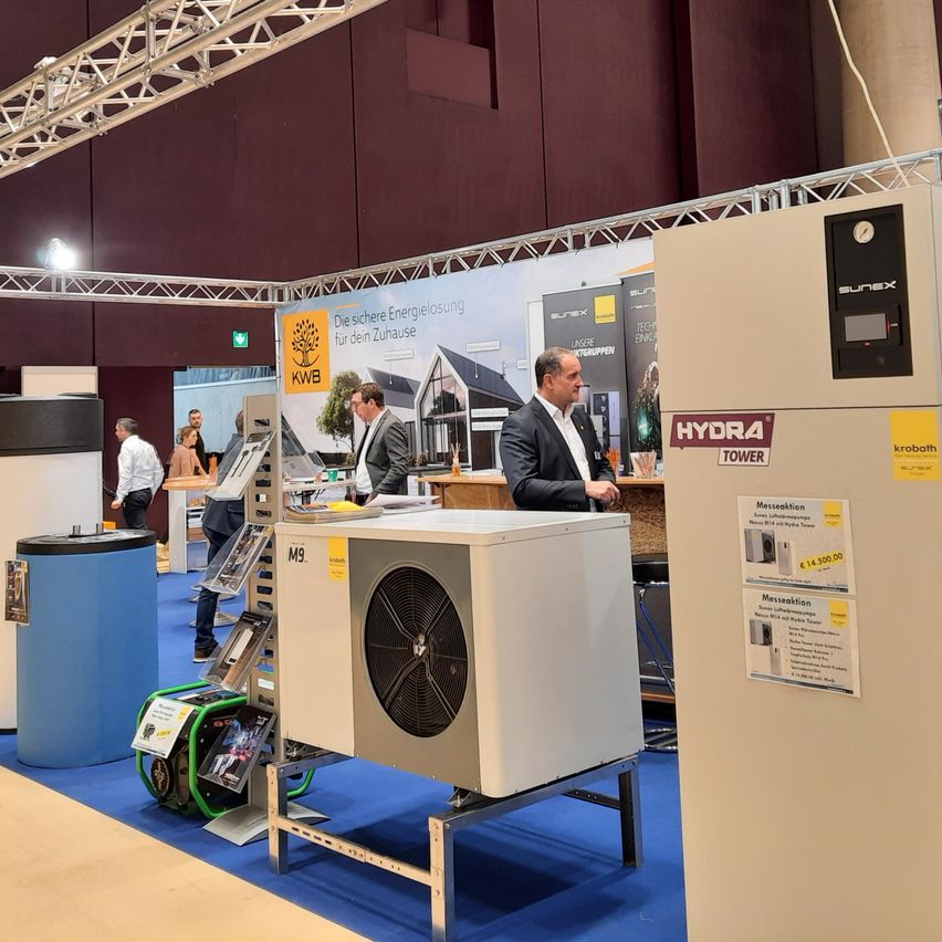 An exhibition with a HYDRA tower and an M9 air conditioning unit on display. People are walking around and examining the equipment.