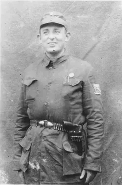 Ein Schwarz-Weiß-Foto eines lächelnden Mannes in Militäruniform, mit einem Gürtel und einer Munitionstasche um die Taille.