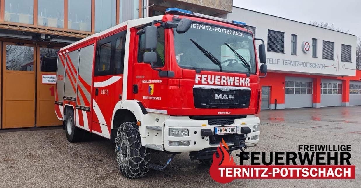 Ein roter Feuerwehrwagen der Feuerwehr Ternitz-Pottschach steht vor einem Gebäude. Der Wagen ist mit Ketten an den Reifen ausgestattet.