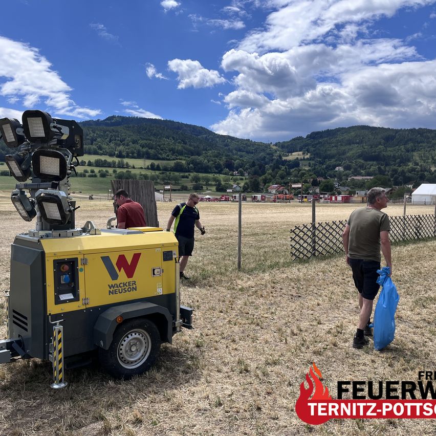 Drei Männer gehen auf einem Feld mit einem Wacker Neuson Generator und einem Zaun im Hintergrund.