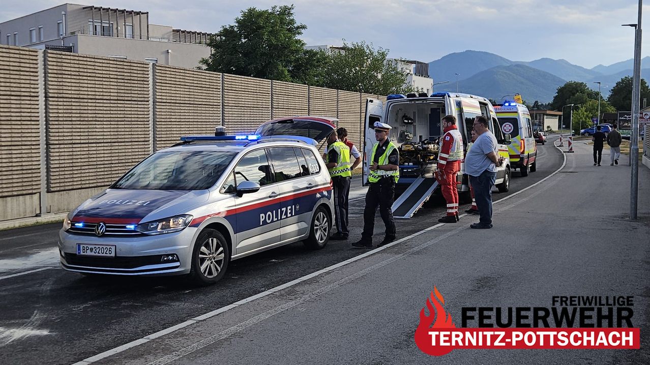 A police car and an ambulance are parked on the side of the road with officers and medics standing around.