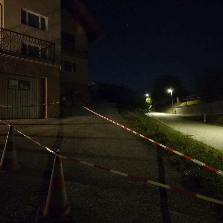 Ein nächtlicher Blick auf eine Straße mit einem Gebäude links, einem abgesperrten Bereich mit Verkehrskegel und Straßenlaternen rechts.