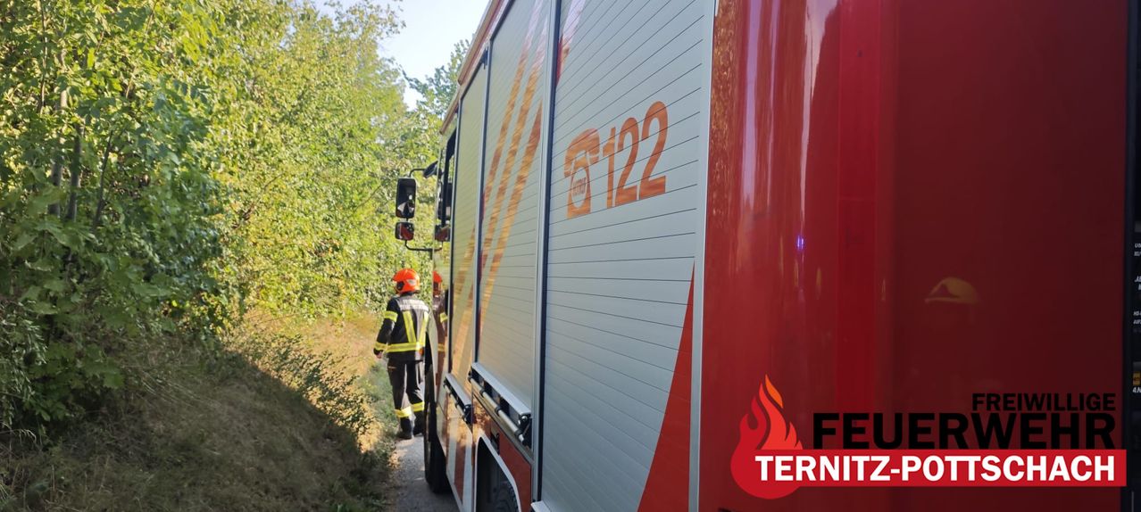 Ein Feuerwehrmann geht auf einen roten Feuerwehrwagen mit der Nummer 5122 zu. Der Wagen steht an einer Straße mit Bäumen an der Seite.