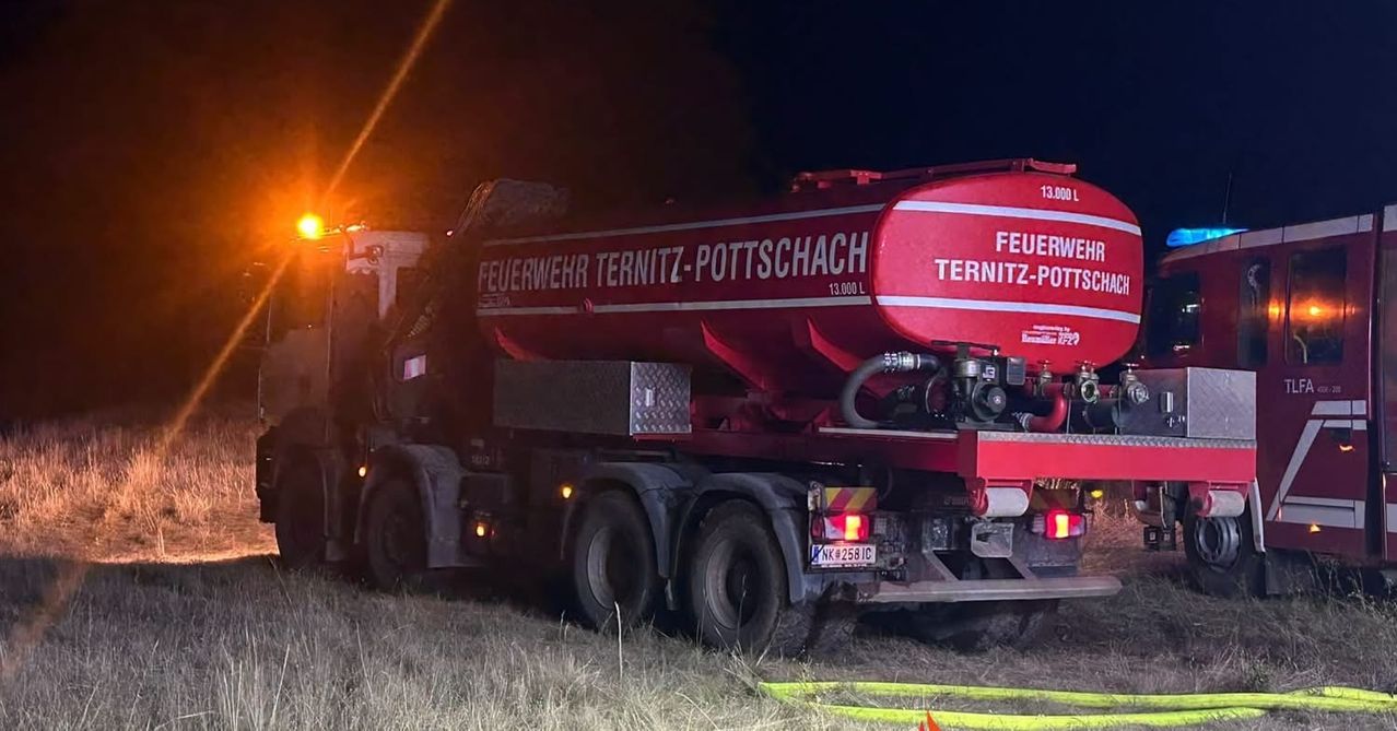 A red fire truck from the Ternitz-Pottschach fire department is parked in a field at night, with its rear end visible and emergency lights on.