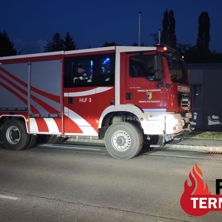 A red fire truck with the number HLF 3 is parked on the side of the road at night. A firefighter is inside the truck, and the emergency lights are on.