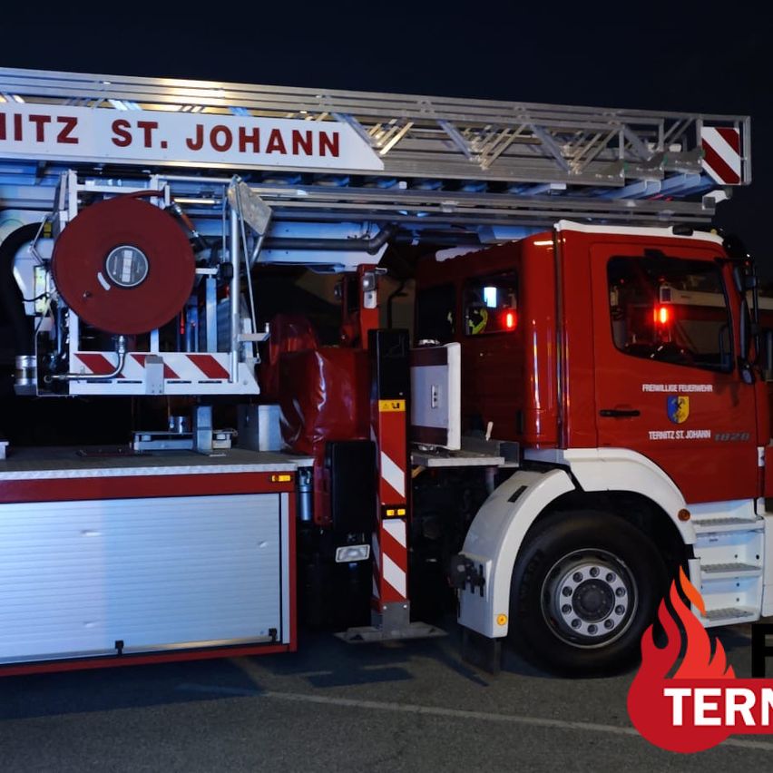 A red fire truck with the words 'WITZ ST. JOHANN' on the ladder is parked at night. The truck has a red hose reel and a fire extinguisher mounted on the side.