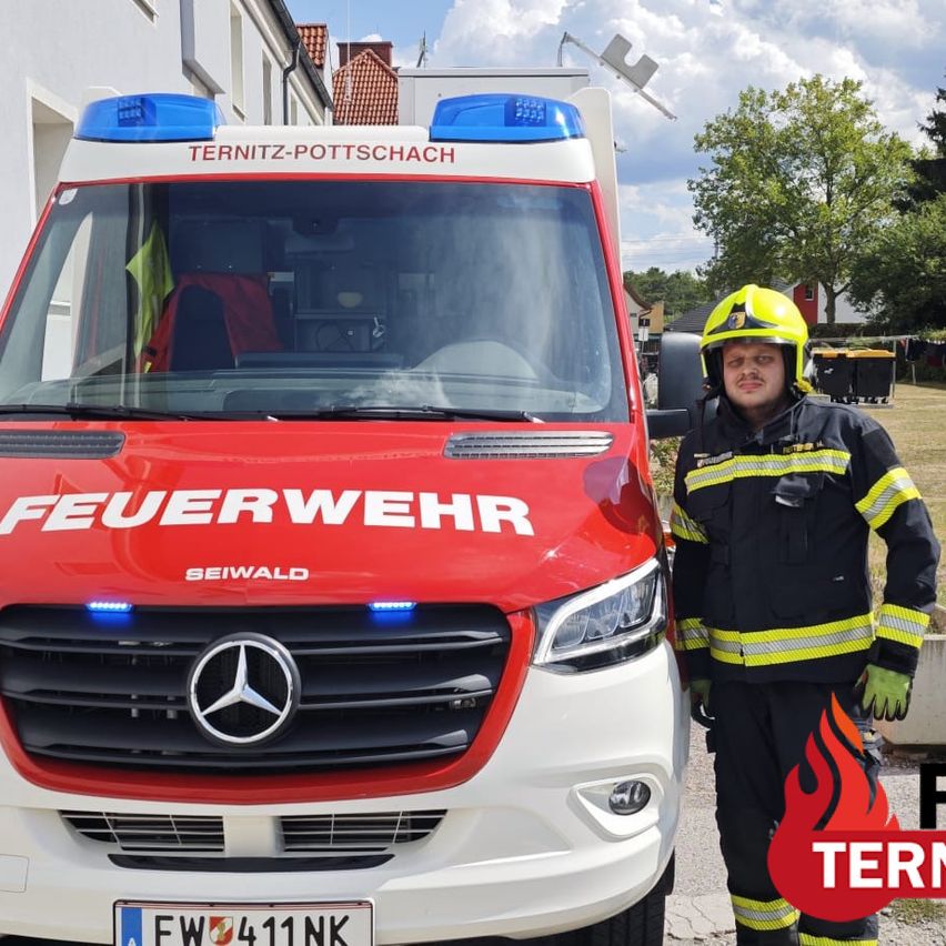 A firefighter stands next to a red and white Mercedes-Benz fire truck with the word 'Feuerwehr' on the front and 'TERNITZ-POTTSCHACH' on the roof.
