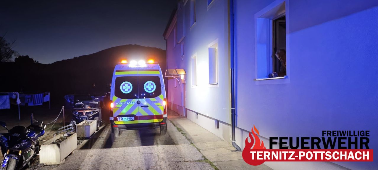 An ambulance with its lights on is parked in front of a building at night.