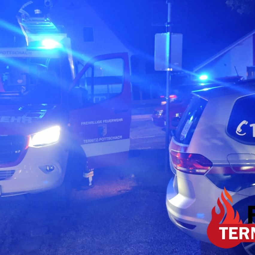 A fire truck with its lights on is parked on the side of the road at night. A car with a fire logo is parked behind it.