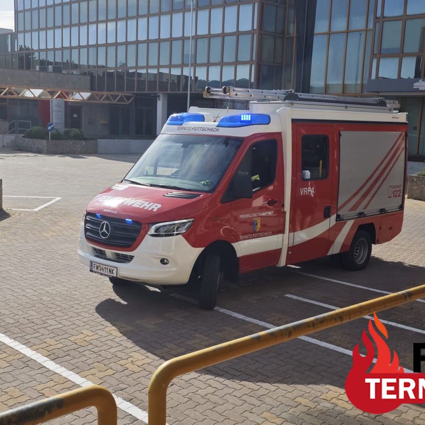 A red and white Mercedes-Benz vehicle with emergency lights on top is parked in a parking lot.