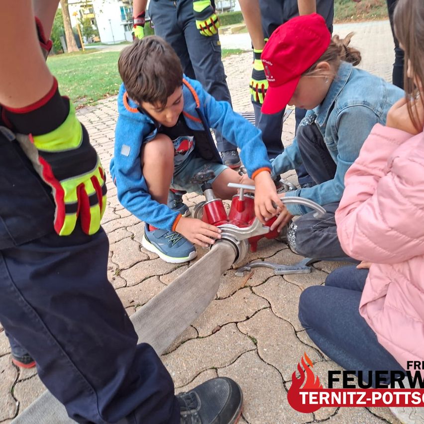 A group of children are learning how to use a fire extinguisher. A boy is holding the nozzle while a girl watches.