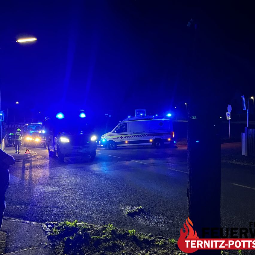 At night, emergency vehicles with blue lights are parked on the side of the road. A person is standing near the vehicles.