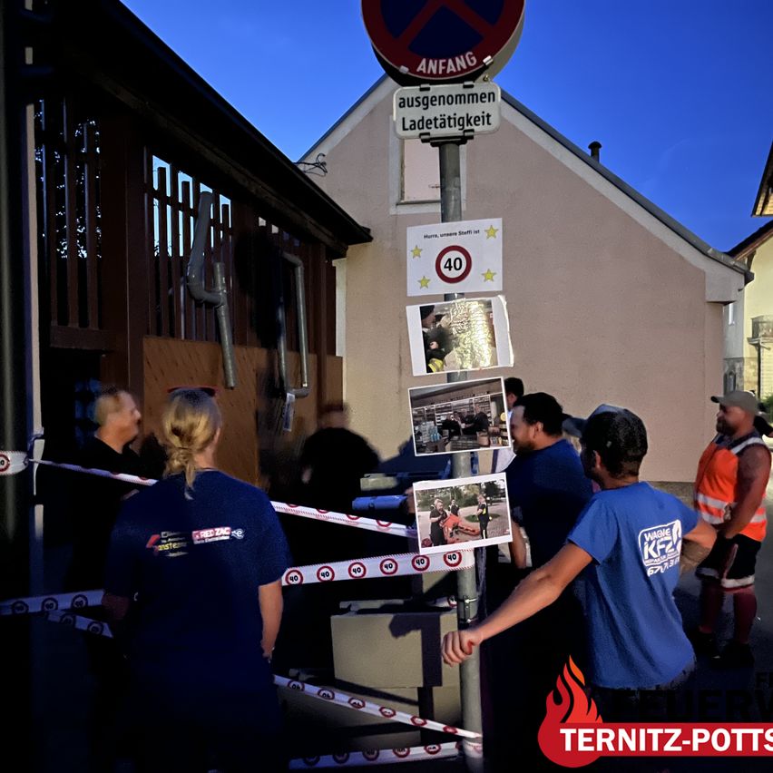 A group of people in blue shirts are standing around a pole with photos and signs. The pole has a speed limit sign of 40 km/h.