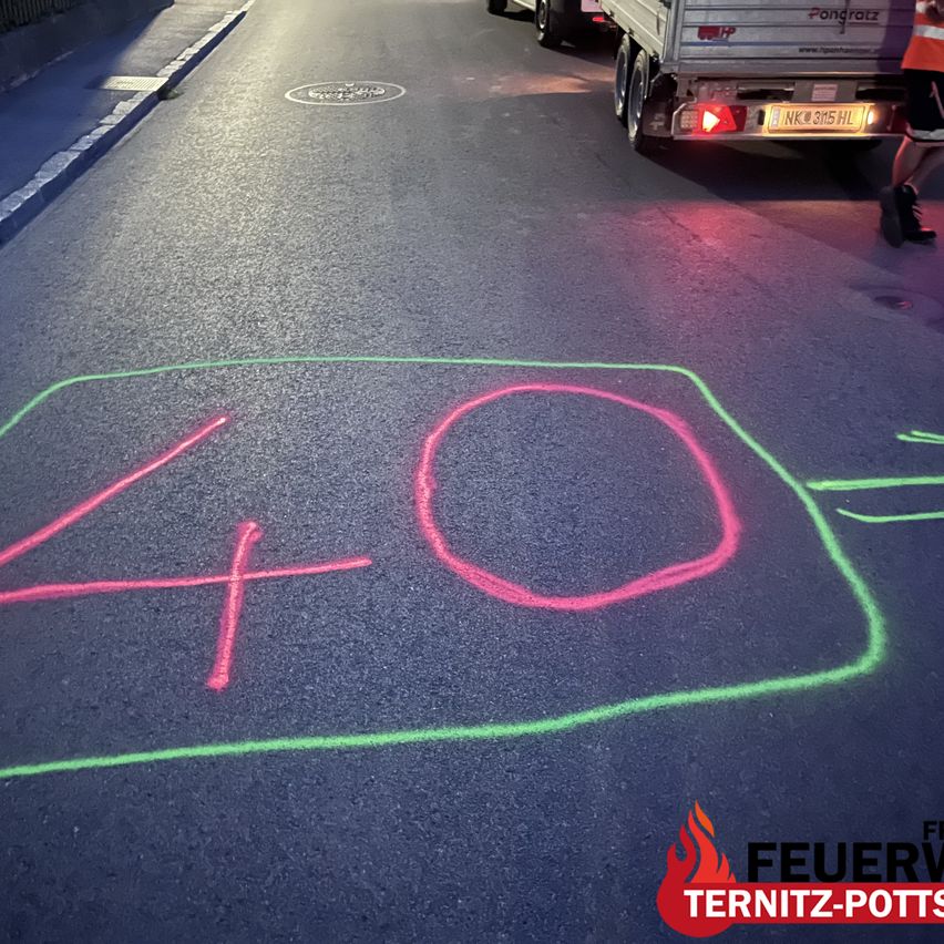 An image shows a road with a chalk drawing of the number 40 on the pavement. A truck is parked nearby, and a person in orange safety clothing is walking on the sidewalk.