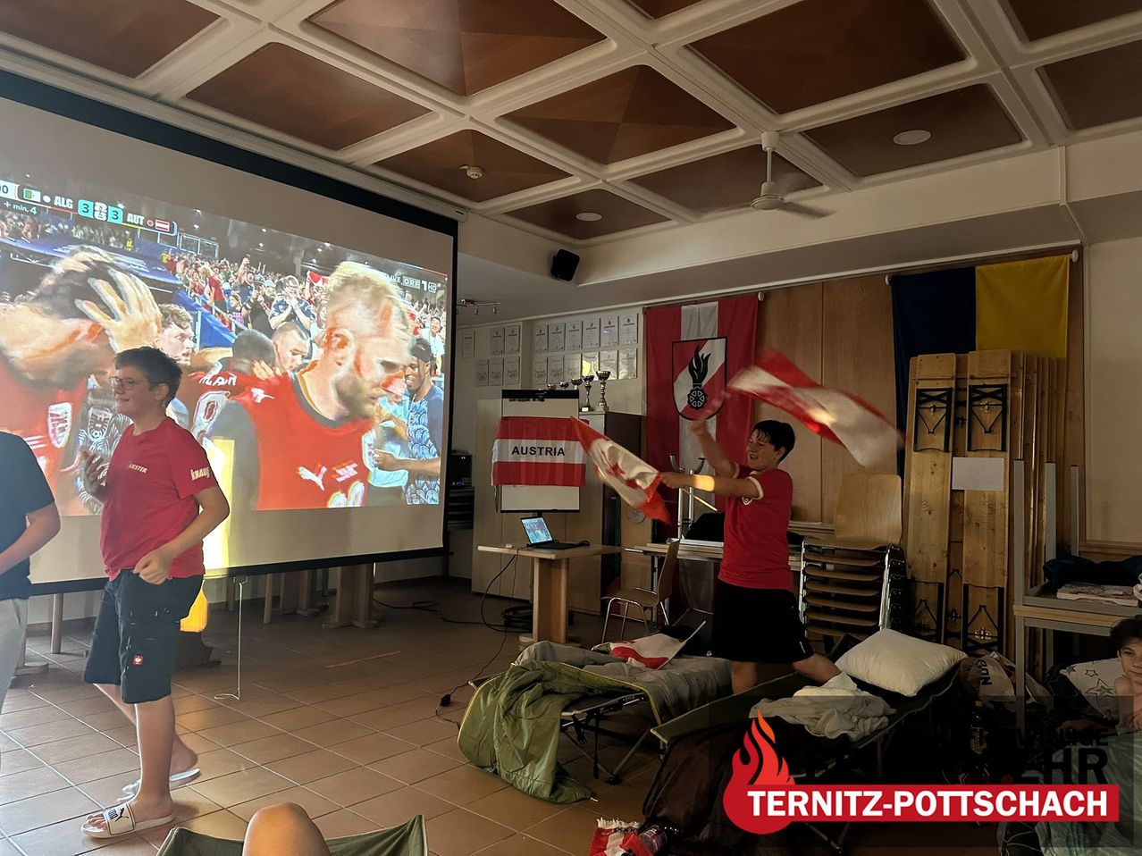 A group of people watching a football match on a projector screen. One person is waving a flag.