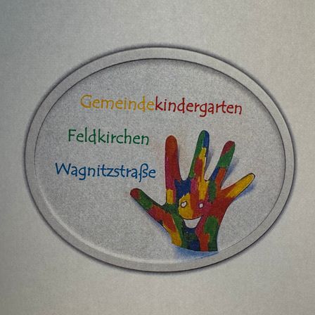 Ein ovaler Aufkleber zeigt einen farbenfrohen Handabdruck mit dem Text 'Gemeindekindergarten Feldkirchen Wagnitzstraße' auf grauem Hintergrund.
