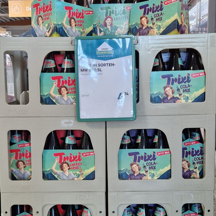 Ein Regal mit Trixie Cola-Mix Flaschen im Laden, mit einem Preisschild, das 74 Euro für eine 6er-Packung 0,5L Flaschen anzeigt.