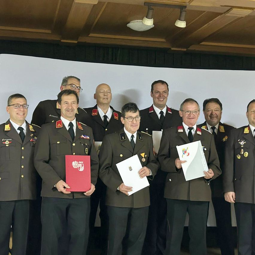 Eine Gruppe von Militäroffizieren in Uniform posiert für ein Foto. Sie halten verschiedene Dokumente in den Händen.