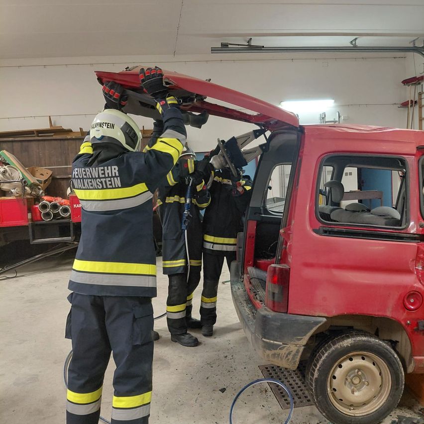 Ein Feuerwehrmann hält das Dach eines roten Lieferwagens, während zwei andere Feuerwehrmänner neben ihm in einer Garage stehen.