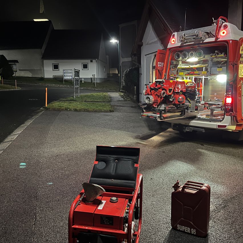 Ein roter Generator steht am Straßenrand, in der Nähe ein roter Feuerwehrwagen. Ein Kraftstoffkanister ist ebenfalls zu sehen.