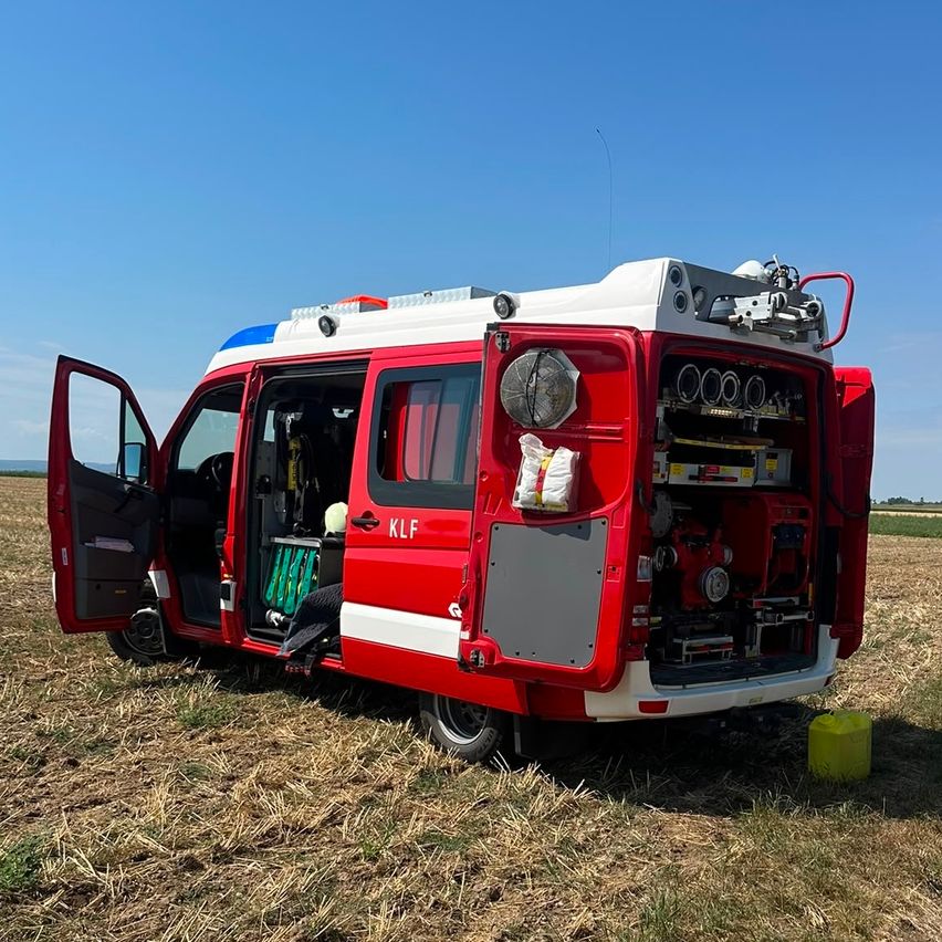 Ein rotes und weißes Notfallfahrzeug mit geöffneten Türen, geparkt auf einem Feld mit einem gelben Behälter in der Nähe.