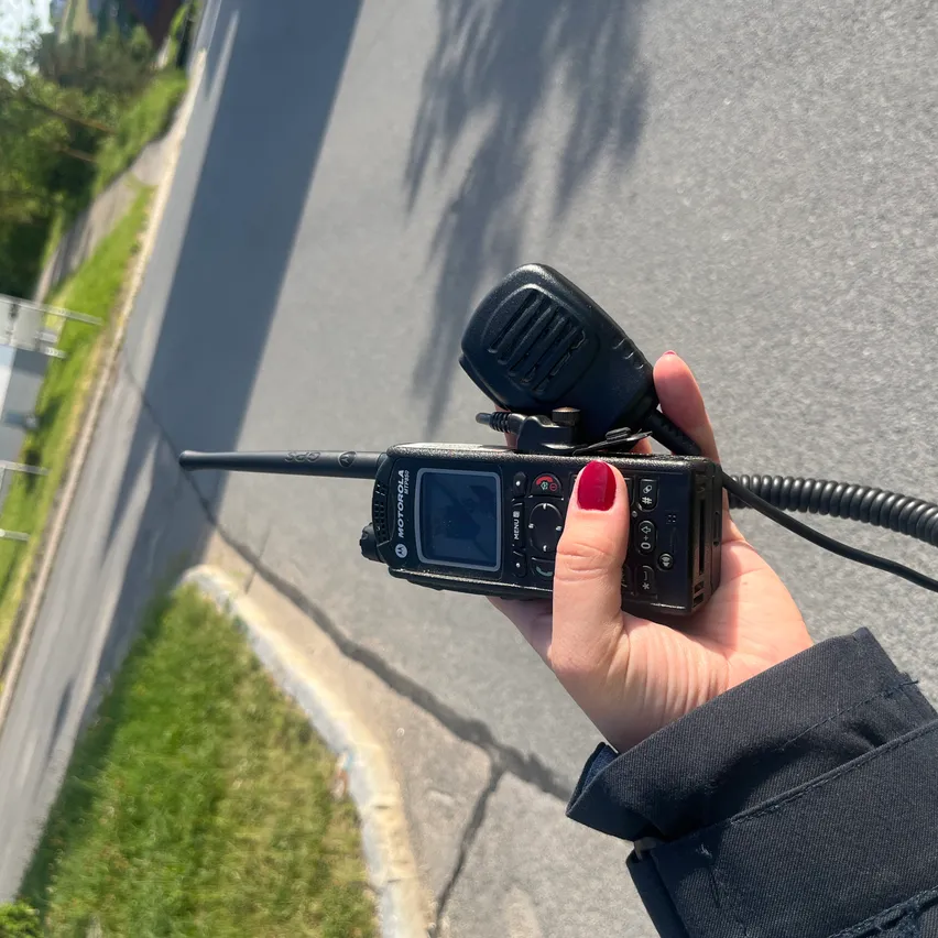 Eine Hand hält ein Motorola-Funkgerät, ein Mikrofon angeschlossen, an einem sonnigen Tag mit einer asphaltierten Straße und Grasrand.